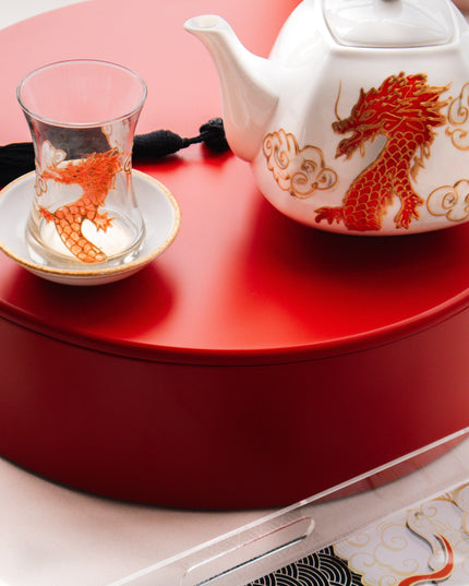 Tea set with teapot and cup on a red surface, tray with dragon design in foreground