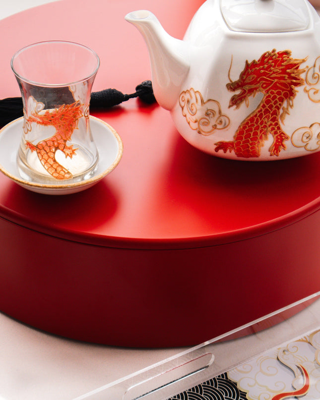 Tea set with teapot and cup on a red surface, tray with dragon design in foreground