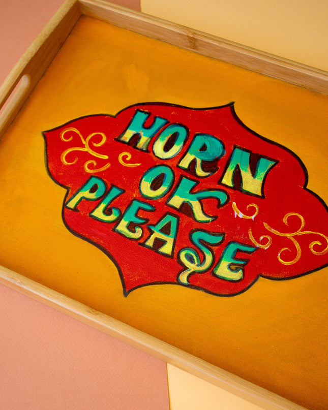 Wooden tray with a colorful sign reading 'Horn Ok Please' on a pink and beige background