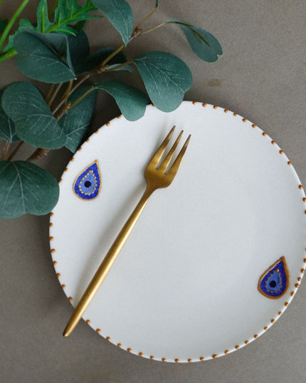 White plate with decorative evil eye blue and gold accents, gold fork on a gray background