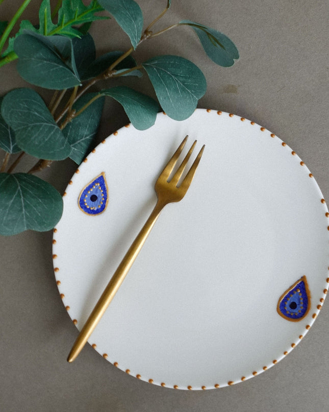 White plate with decorative evil eye blue and gold accents, gold fork on a gray background