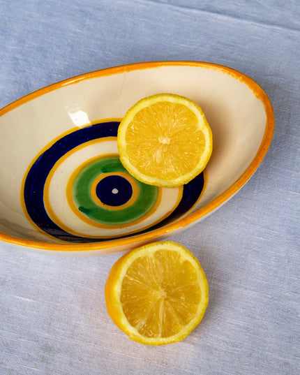 Sliced lemons on a decorative ceramic bowl with hand-painted evil eye design on a gray surface