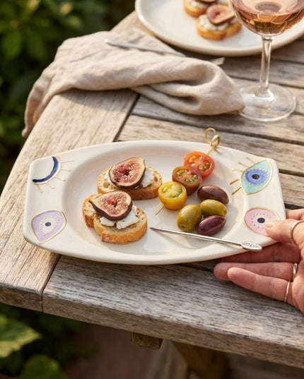 Hand holding a Rangeela evil eye appetizer plate serving appetizers on a wooden table