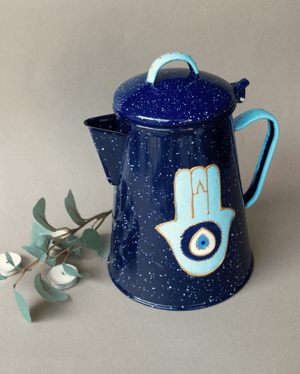 Blue metal teapot with Hamsa design on a beige background