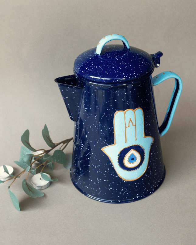 Blue metal teapot with Hamsa design on a beige background