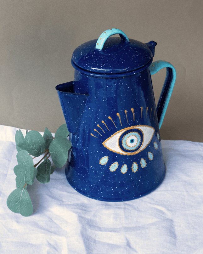 Blue metal teapot with eye design on a white surface