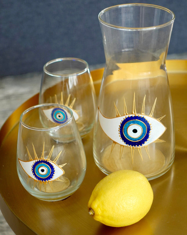 Set of glass tumblers and carafe with eye designs on a gold tray with a lemon.