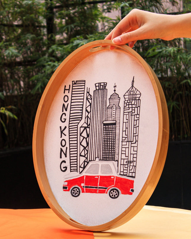 Oval-shaped tray with a red HK Taxi and cityscape design, held by a hand on an orange and yellow background.