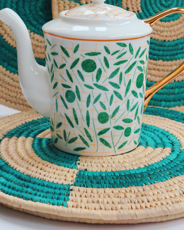 Teapot with green leaf pattern on green woven grass placemats