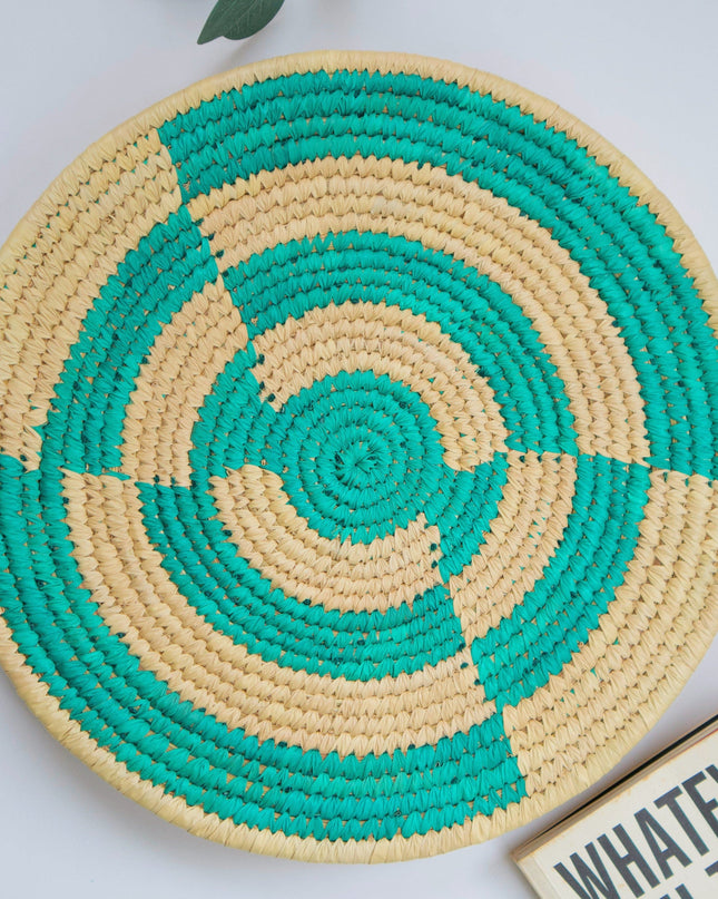 Round woven mat with green and beige spiral pattern on a light background