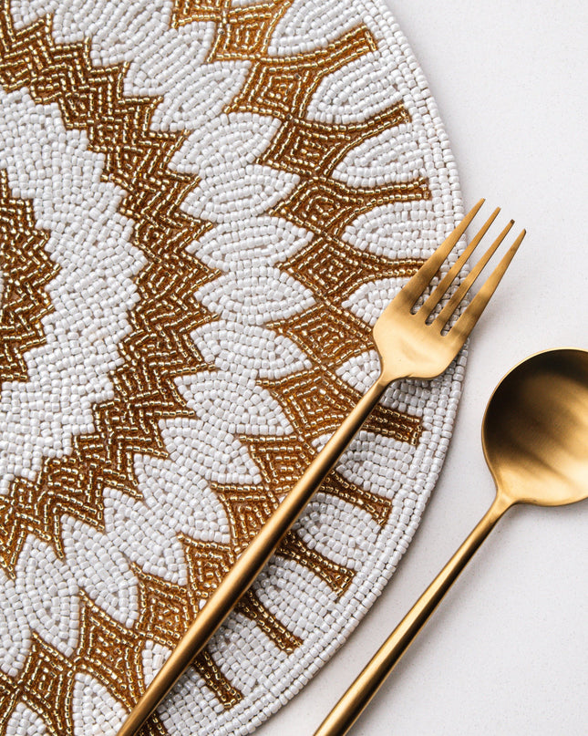 Gold fork and spoon on a decorative beaded placemat with intricate patterns
