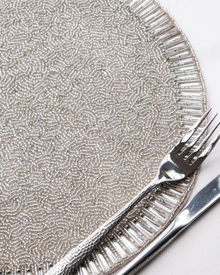 Silver beaded placemat with a fork and knife on a white background