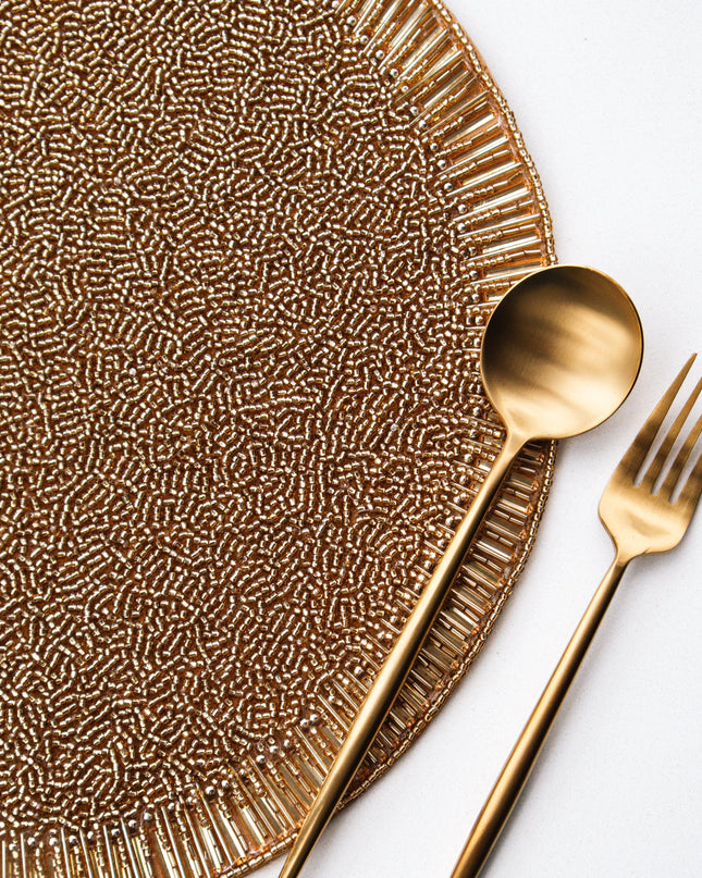 Gold beaded placemat with matching spoon and fork on a white background