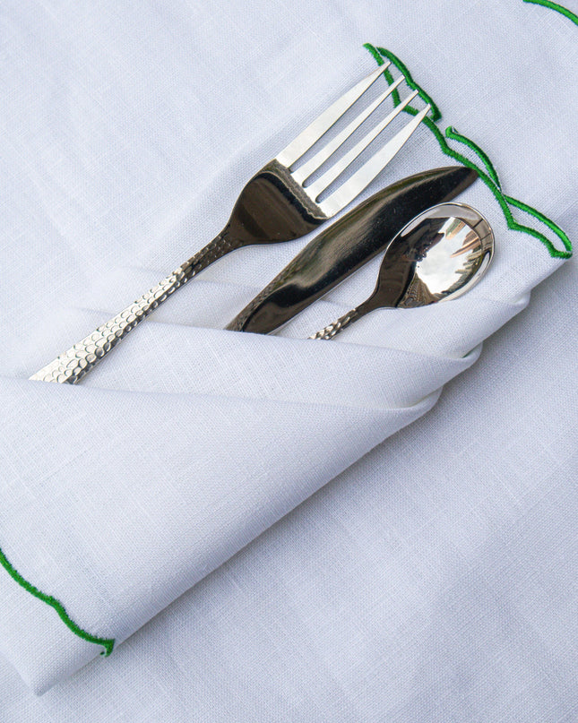 Silverware on a white placemat and napkin with green embroidery