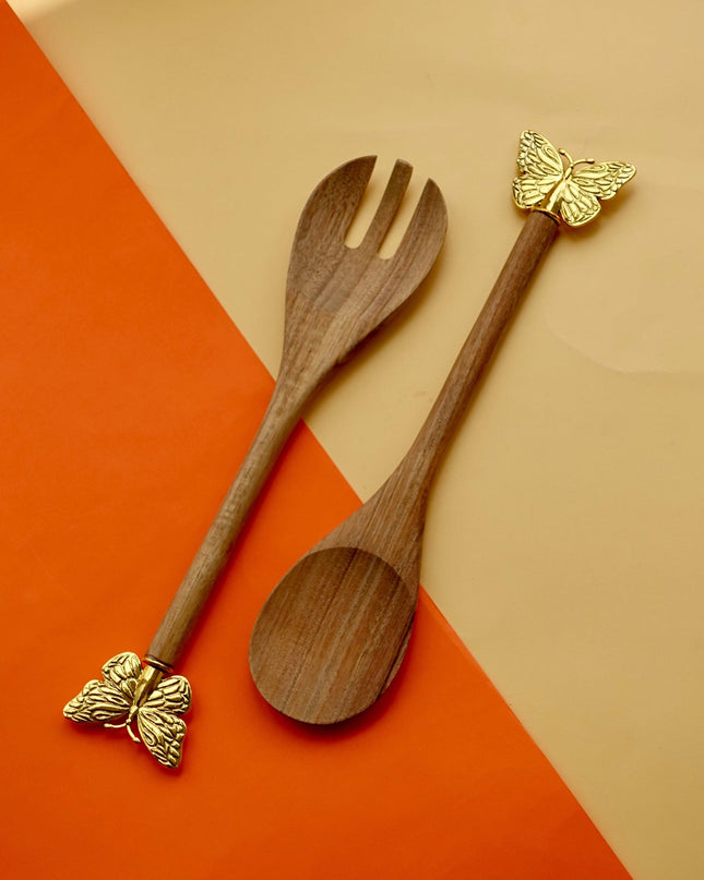 Wooden salad servers with gold butterfly ends on a two-tone orange and beige background