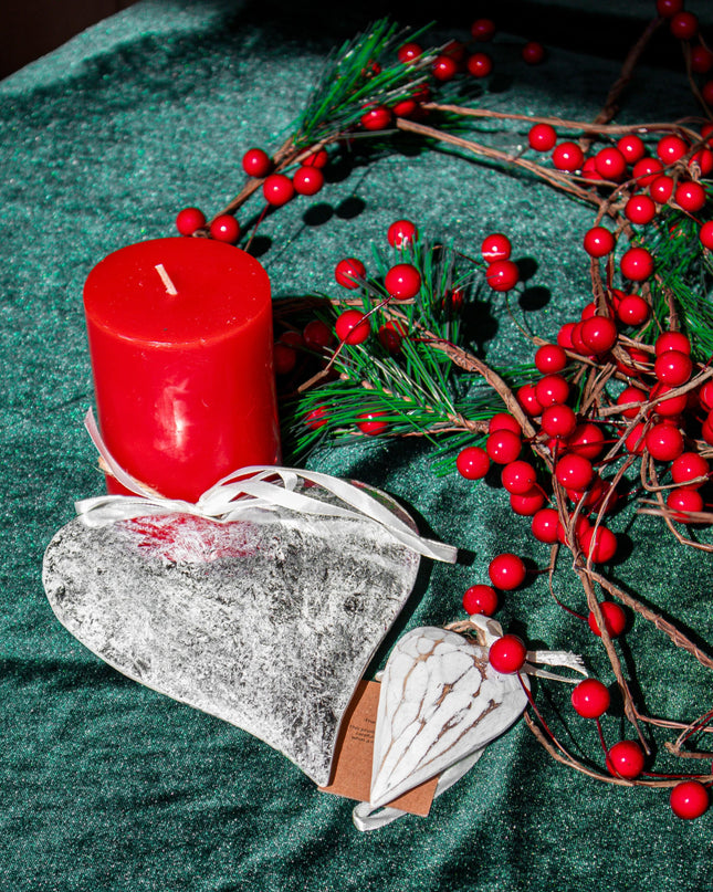 Red candle, heart-shaped ornaments and decorative branches on a green surface