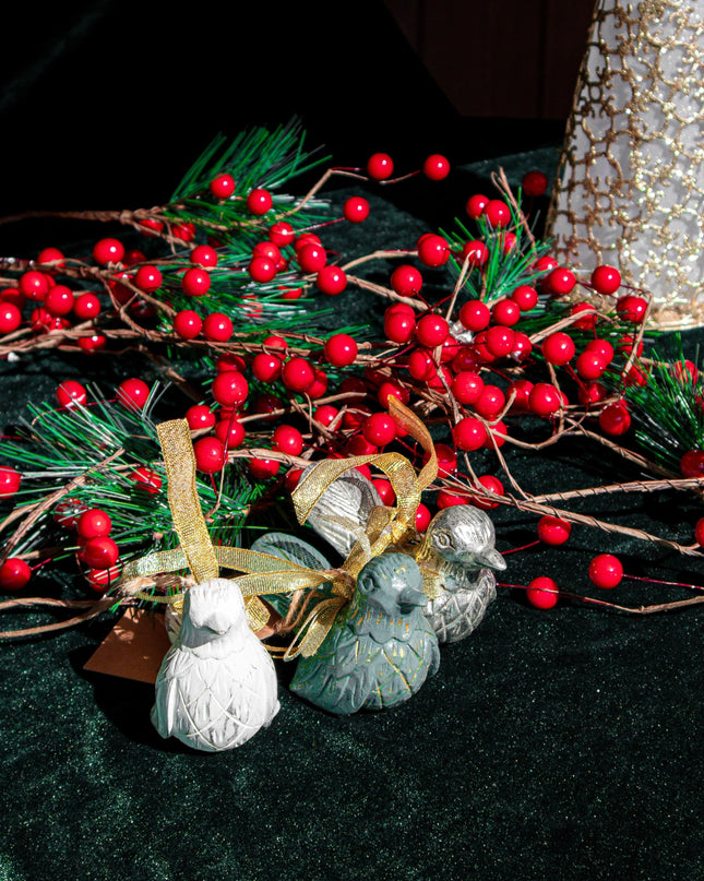 Decorative Christmas bird ornaments with red berries, greenery, and small ornaments on a dark surface
