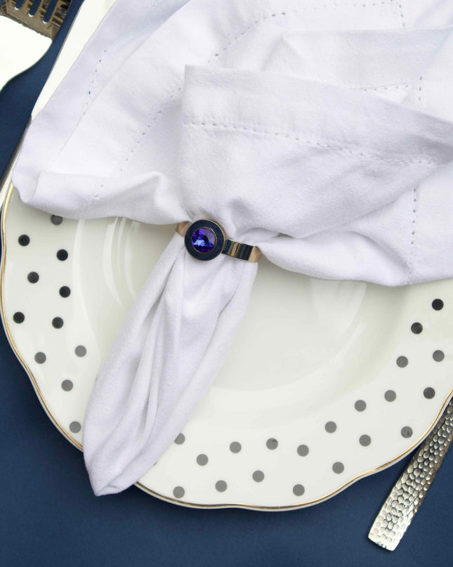 White folded napkin with a blue napkin ring on a polka dot plate against a dark background