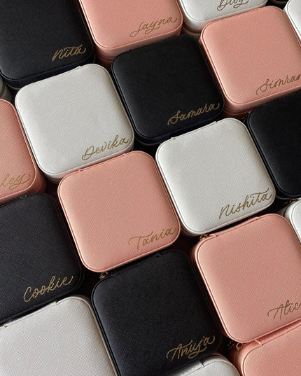 Collection of small square jewelry boxes in various colors with names engraved on them.