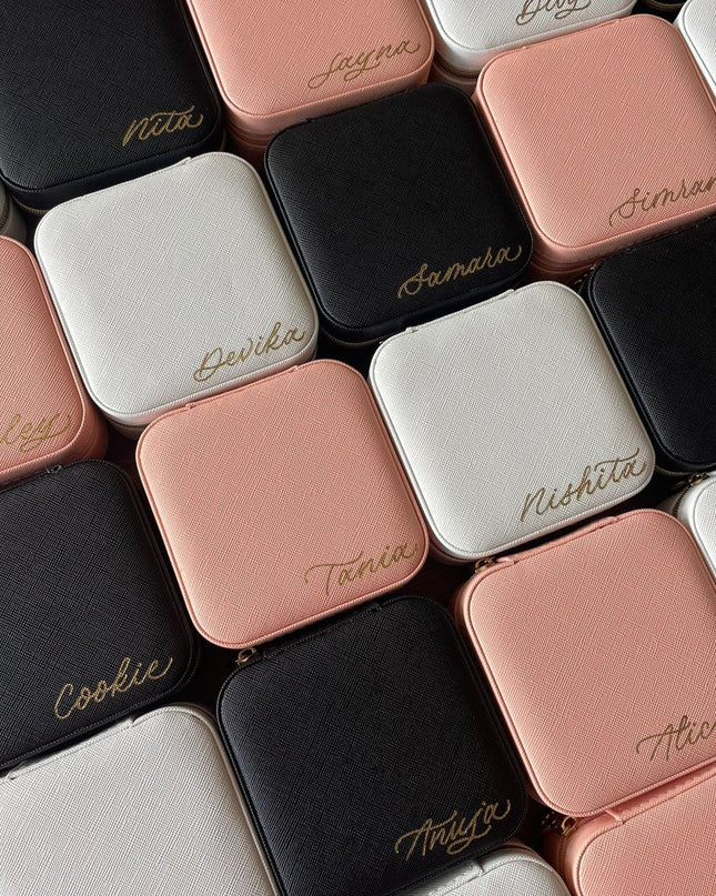 Collection of small square jewelry boxes in various colors with names engraved on them.