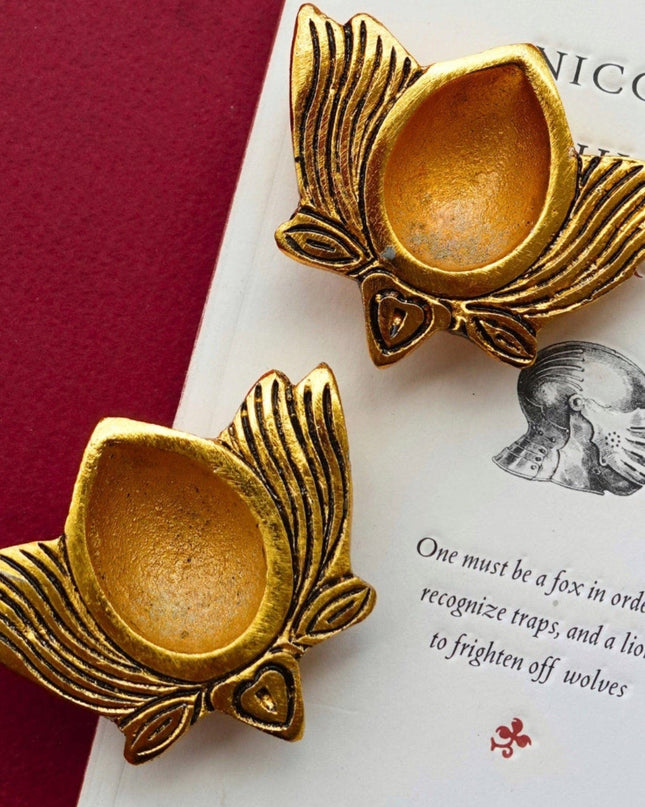Two gold lotus-shaped diya holders on a book with text.