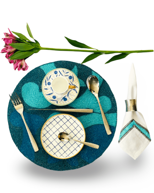 Blue Beaded Placemat with Nadia Dafri Turquoise Embroidered Napkin and White and Blue Teacup with Dessert Plate, Hammered Silver Cutlery Set and Napkin Ring and  pink flower