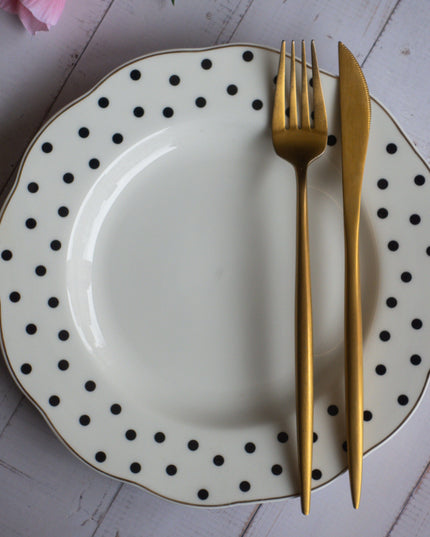Polka dot plate with gold fork and knife on a white wooden surface with pink flowers.