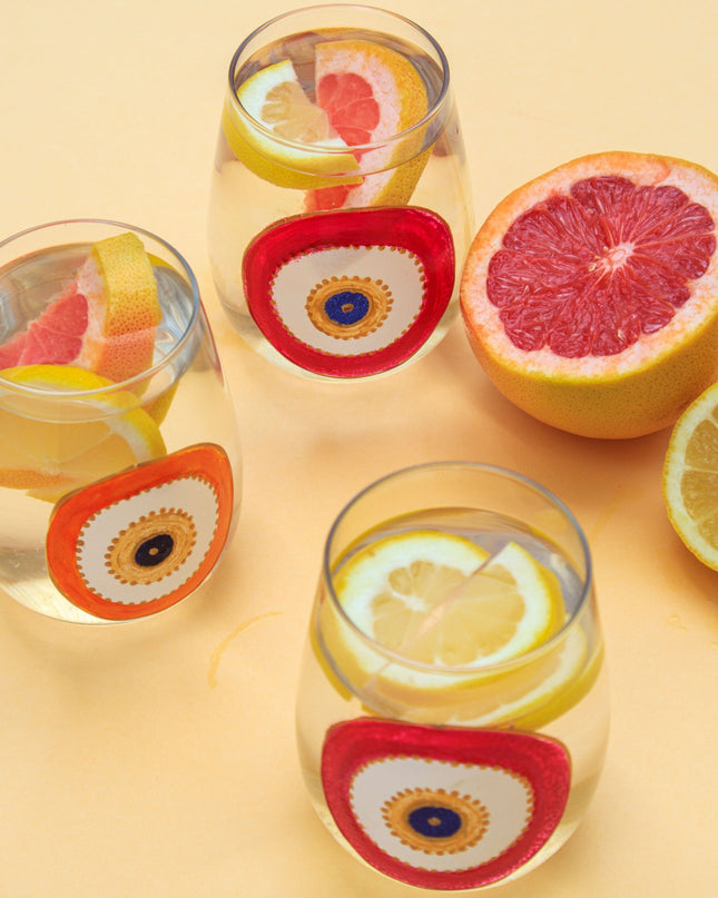 Clear glasses with hand-painted evil eye designs and fruit slices on a yellow background