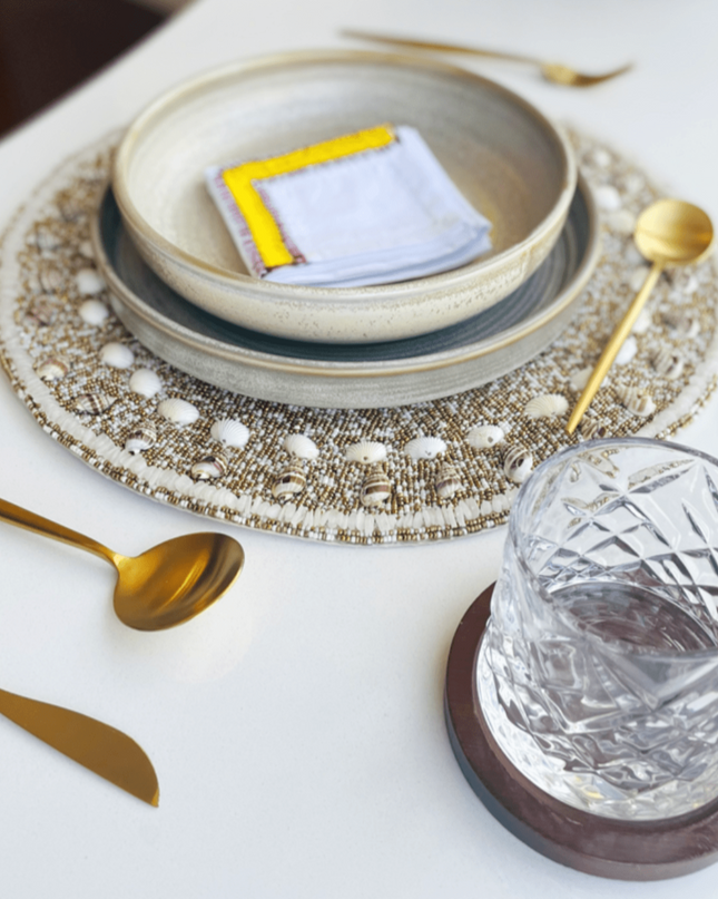 Nadia Dafri White Cotton Embroidery Yellow Napkin Beaded Placemat with Shells Gold Rustic Dinner Plate Gold Cutlery Whiskey Glass